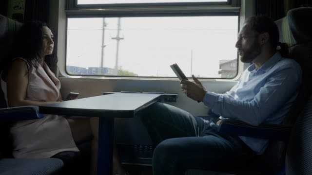 Corporate-employees-man-and-woman-or-coworkers-enjoying-conversation-while-they-using-their-gadget-on-train-compartment-commuting-to-office
