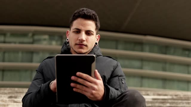 Hombre-joven-reflexivo-usando-la-tableta-mientras-que-se-sienta-al-aire-libre.