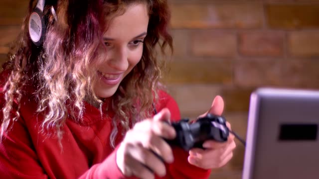 Close-up-portrait-of-young-female-blogger-actively-playing-video-game-using-joystick-on-bricken-wall-background.