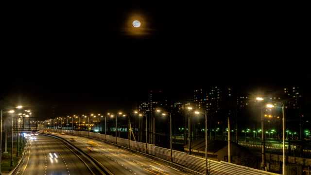 The-moon-rising-over-the-illuminated-highway-and-the-night-city,-time-lapse