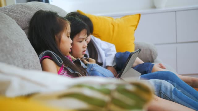 Group-of-kids-playing-with-digital-tablet-together-on-sofa-at-home,-and-smiling,-kids-on-digital-tablet-in-living-room,-Tilt-up-shot.