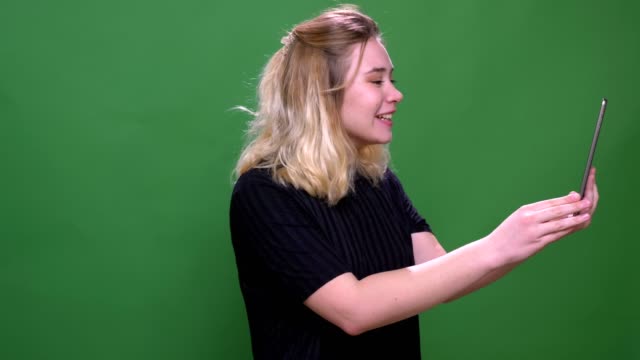 Nahaufnahme-Porträt-von-jungen-hübschen-blonden-kaukasischen-Frau-mit-einem-Videoanruf-auf-dem-Tablet-mit-Hintergrund-isoliert-auf-grün
