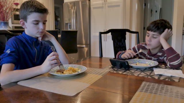 Zwei-junge-Jungen-essen-Frühstück,-während-man-Videos-auf-einem-Smartphone-ansieht