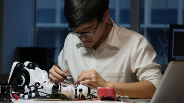 Un-joven-ingeniero-electrónico-asiático-trata-de-arreglar-el-robot-en-el-laboratorio.-Concepto-de-tecnología-e-innovación.