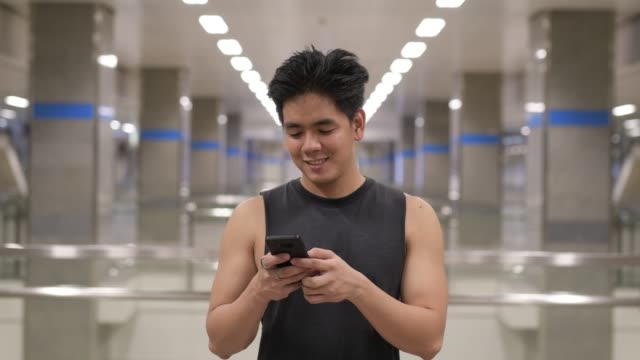 Joven-feliz-asiático-usando-el-teléfono-en-la-estación-de-metro