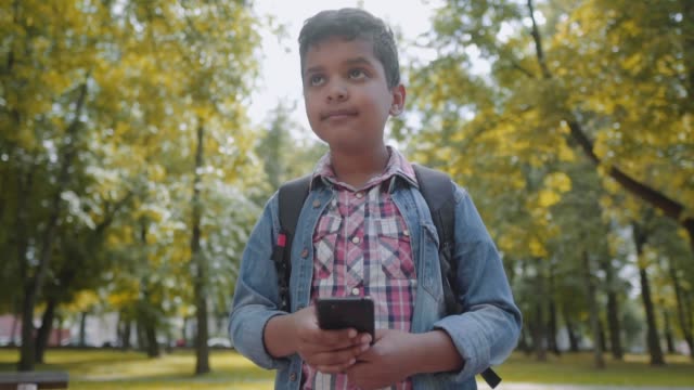 Outdoor-portrait-afro-american-happy-school-boy-with-smartphone.-Young-student-looking-at-mobile-phone.-Back-to-school-concept.-Slow-Motion-Shot