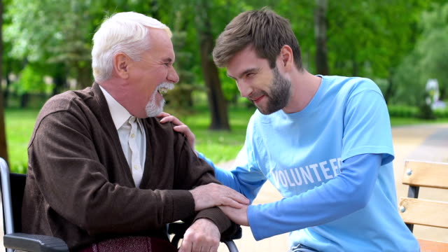 Männlicher-Freiwilliger-und-älterer-behinderter-Mann-lacht-im-Park,-einsame-Rentner-kümmern-sich