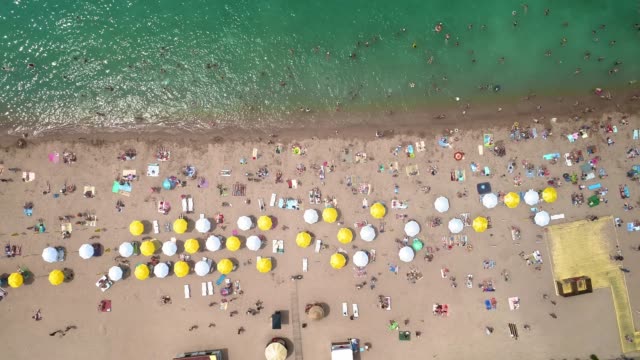 Luftaufnahme:-Top-Ansicht-des-Strandes.-Menschen-baden-im-Meer,-am-Ufer-holzige-Sonnenschirme