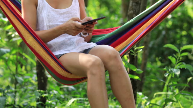 Woman-relaxing-in-hammock--reading-ebook-in-tropical-rainforest
