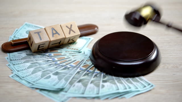 Dollars-and-tax-word-made-of-wooden-cubes-table,-gavel-striking-on-sound-block