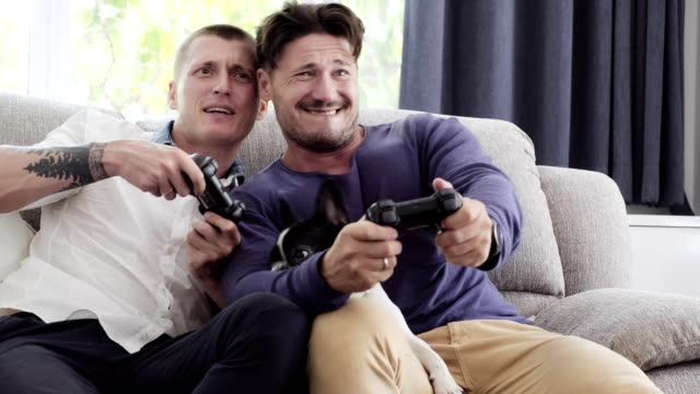Gay-couple-relaxing-on-couch-with-dog-playing-games.-Having-fun.