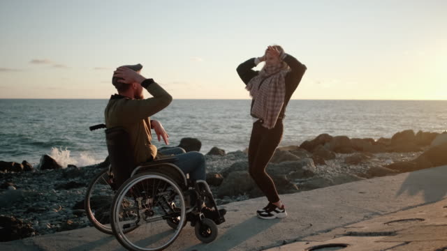 Cheerful-disabled-man-and-woman-are-having-fun-and-dancing-on-sea-embankment