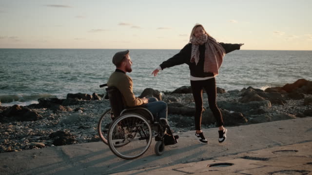 Behinderter-Mann-und-seine-gesunde-Freundin-haben-Spaß-am-Meer,-tanzen