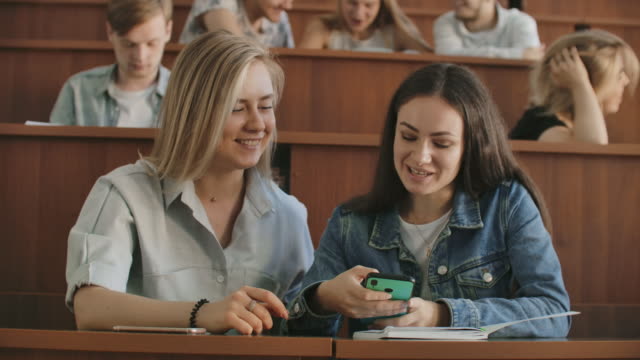 Female-students-with-a-smartphone-in-their-hands-laughing-in-the-audience-during-a-break-for-a-lecture-at-the-University