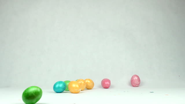 Los-huevos-de-Pascua-multicolores-caen-sobre-la-mesa,-la-piel-se-rompe,-el-fondo-blanco-es-el-concepto-del-final-de-las-vacaciones,-cámara-lenta,-espacio-de-copia,-fondo