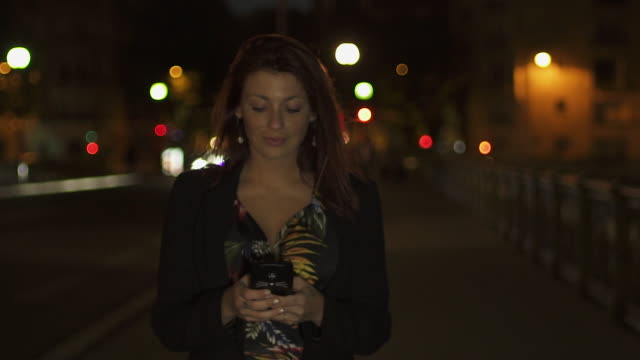 Schöne-attraktive-kaukasische-moderne-Frau-trägt-Blumenkleid,-schwarze-Jacke-und-rote-Haare-zu-Fuß-durch-die-Straße-und-schreiben-eine-SMS-auf-ihrem-Smartphone-in-der-Nacht.-Paris-4K-UHD.-Zeitlupe.