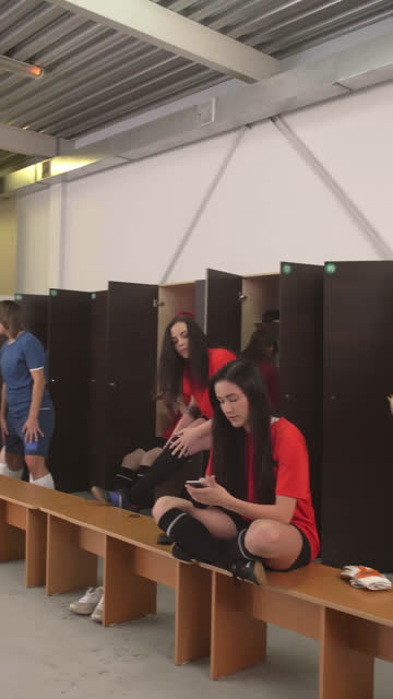 Female-Soccer-Player-Using-Smartphone-and-Making-Ponytail-in-Locker-Room