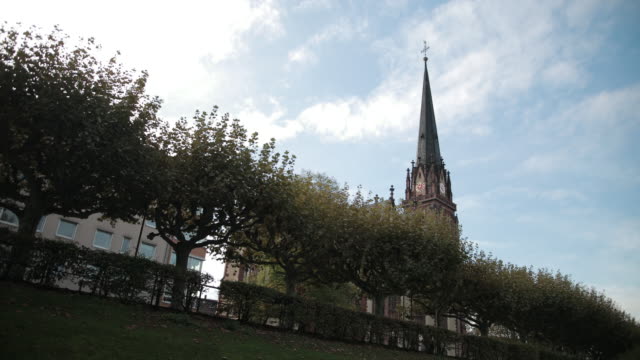 Alte-Kirche-im-gotischen-Stil.-Mit-spitzem-Dach-und-Uhr.-Im-Vordergrund-stehen-Bäume