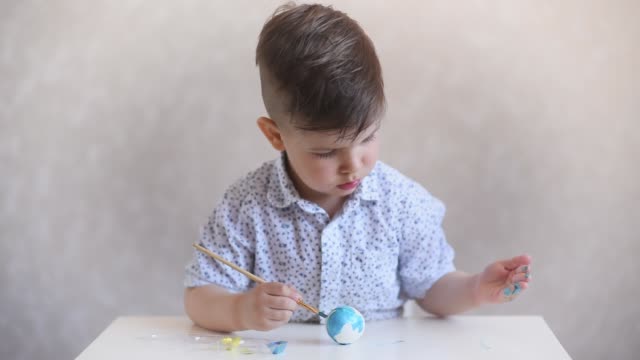 Un-niño-pinta-un-huevo-de-pascua-en-la-mesa-sobre-un-fondo-blanco.