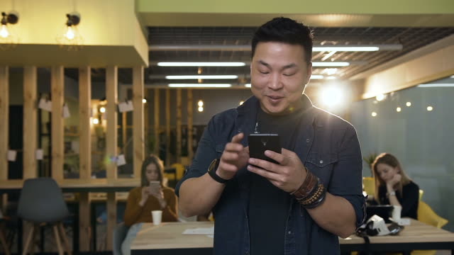 Junge-korean-Mann-mit-Smartphone-auf-modernem-Büro-Hintergrund