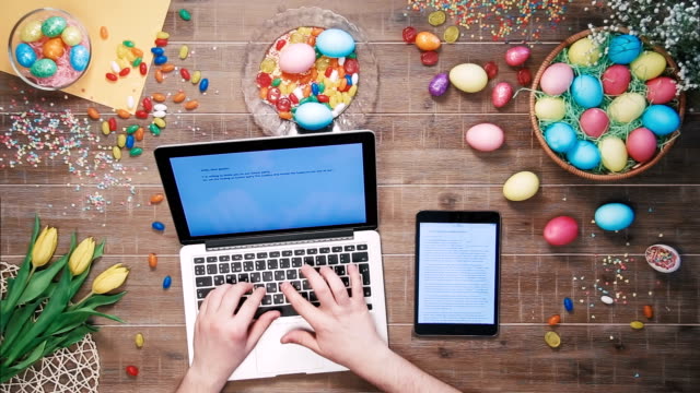 Hombre-con-ayuda-de-ordenador-portátil-y-tableta-digital-en-mesa-decorada-con-vista-superior-de-huevos-de-Pascua