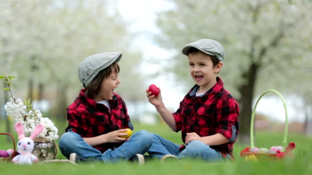 Dos-niños,-hermanos-niño,-divertirse-con-los-huevos-de-Pascua-en-el-parque,-jardín-floreciente-de-hermosa-primavera