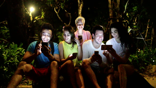 Menschen-gruppen-mit-Handy-Smartphone-sitzen-auf-Bank-im-Abendpark,-junge-Freunde-sprechen-Networking-Online