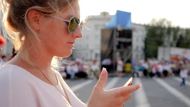 women-blonde-in-glasses-looks-in-phone-on-open-air-at-downtown-close-up