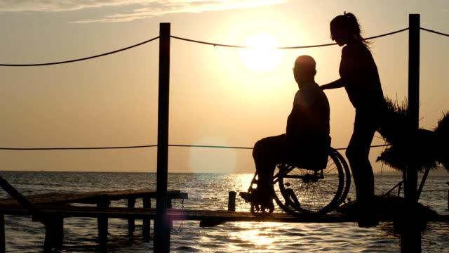 schöne-Mädchen-sprechen-mit-glücklichen-Menschen-mit-Behinderungen-und-suchen-in-der-Skyline-im-Hintergrund-des-Sonnenuntergangs-über-Fluss