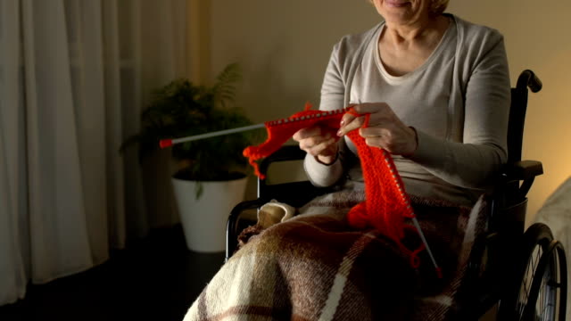 Happy-woman-in-wheelchair-knitting,-thinking-about-grandchildren-and-smiling