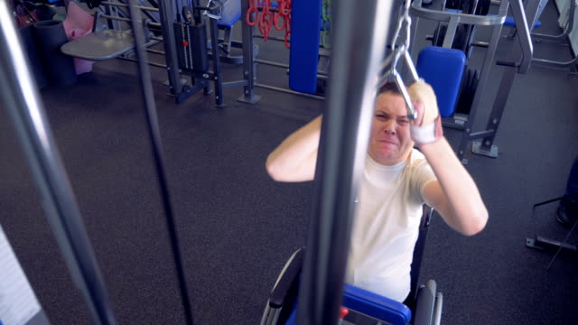 A-disabled-man-is-lifting-weights-in-a-gym-holding-a-metal-handle-by-both-of-his-hands
