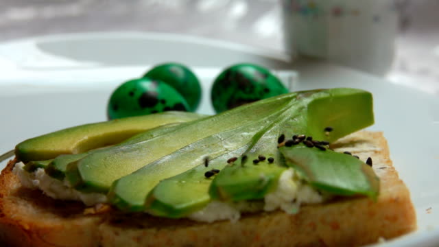 Sandwich-mit-Avocado-bestreut-mit-schwarzem-Sesam-auf-einem-Hintergrund-von-Easter-eggs