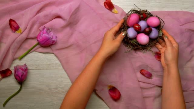 Hands-put-on-the-table-an-Easter-nest-with-colored-eggs-and-a-tray-with-tea