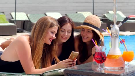 hen-party,-girlfriends-are-sitting-into-social-networks-on-smartphone-near-Swimming-pool-and-Colored-Cocktails