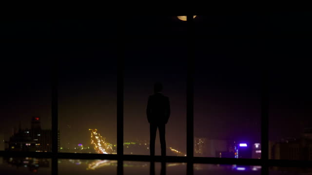 El-hombre-pie-cerca-de-una-ventana-panorámica-en-el-fondo-de-la-ciudad-de-noche