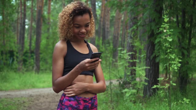 young-beautiful-African-American-woman-with-curly-hair-is-chatting-in-her-phone-before-jogging