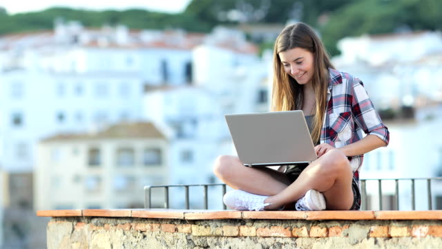 Happy-Teen-schreiben-auf-einem-Laptop-in-den-Urlaub