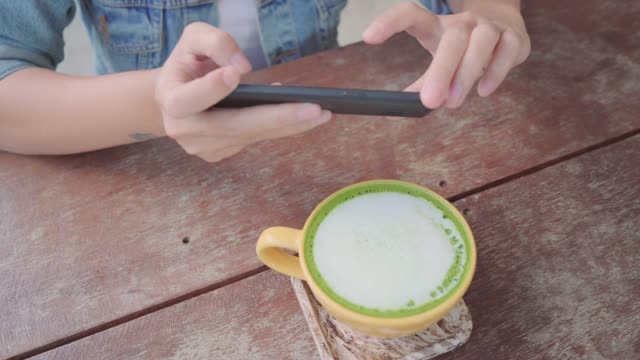 Bloggerin-Tasse-grüner-Tee-im-Café-mit-ihrem-Telefon-zu-fotografieren.-Eine-junge-Frau-nehmen-Foto-von-Kaffee-Tee-auf-Smartphone,-Mahlzeit-mit-Handy-Kamera-fotografieren.