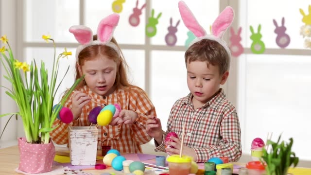 Happy-children-wearing-bunny-ears-painting-eggs-on-Easter-day.-Little-girls-preparing-for-the-Easter.