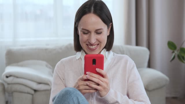 Mujer-riendo-mientras-usa-el-teléfono-móvil-en-casa