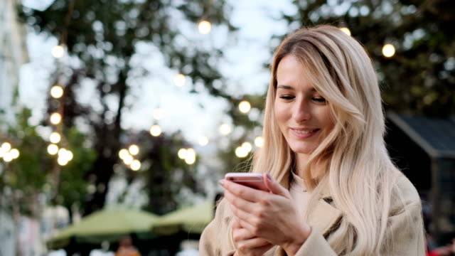 Beautiful-woman-using-smart-phone-technology-app-walking-through-city-streets.-Girl-scrolls-through-social-media-on-device,-reading-news-on-app.