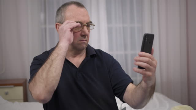 Ein-älterer-Mann-mit-Brille-versucht,-etwas-im-Telefon-zu-sehen