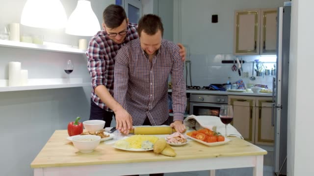 Couple-of-men-gay-roll-out-the-pizza-dough-together-hugging.