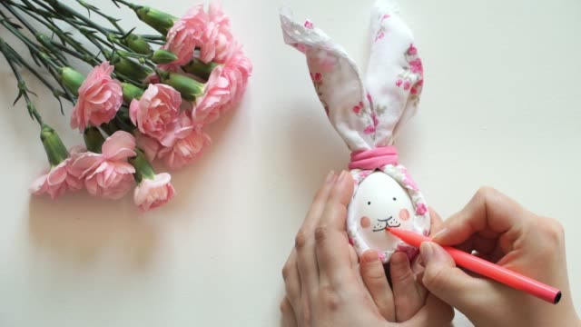 Women's-and-children's-hands-hold-chicken-egg-decorated-for-Easter-bunny,-paint-rabbit's-face-with-pink-marker.