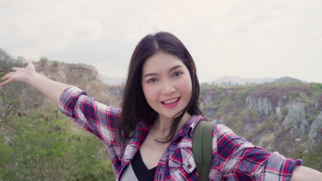 Blogger-Asian-backpacker-woman-record-vlog-video-on-top-of-mountain,-young-female-happy-using-mobile-phone-make-vlog-video-enjoy-holidays-on-hiking-adventure.-Lifestyle-women-travel-and-relax-concept.