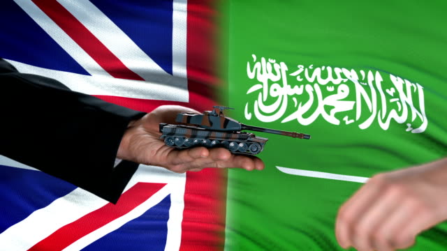 Great-Britain-and-Saudi-Arabia-officials-exchanging-tank-money,-flag-background