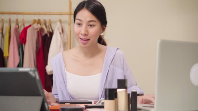 Beauty-blogger-question-and-answer-by-laptop-sitting-in-front-tablet-for-recording-video.-Happy-beautiful-young-Asian-woman-use-cosmetics-review-make-up-tutorial-broadcast-live-video-to-social-network