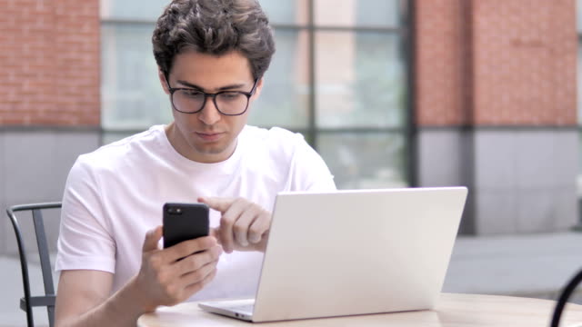 Junger-Mann-mit-Smartphone-und-Laptop-im-Freien