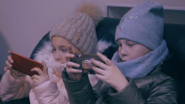 Two-teenager-girls-in-winter-clothes-watching-mobile-phones-and-playing-in-game