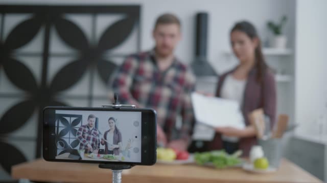 gesunder-Lebensstil,-Blogger-Frau-und-Mann-bereiten-nützliches-Mittagessen-mit-Gemüse-und-Grüns-in-der-Küche,-während-Kamera-Smartphone-Zeichnet-Video-für-Abonnenten-in-sozialen-Netzwerken